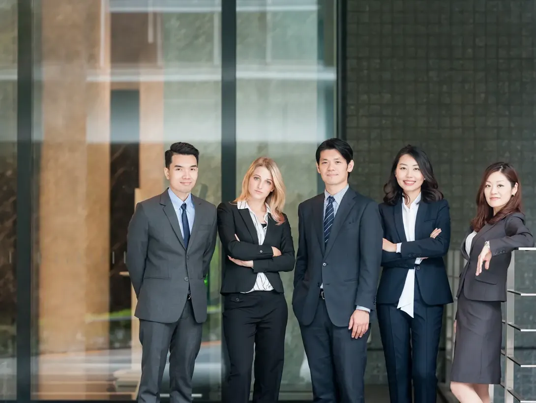 Five diverse business professionals in suits standing confidently outside a modern building.