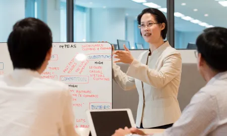 A woman presents a business strategy whiteboard, featuring terms like substitutes, competition, and buyers, to two people.