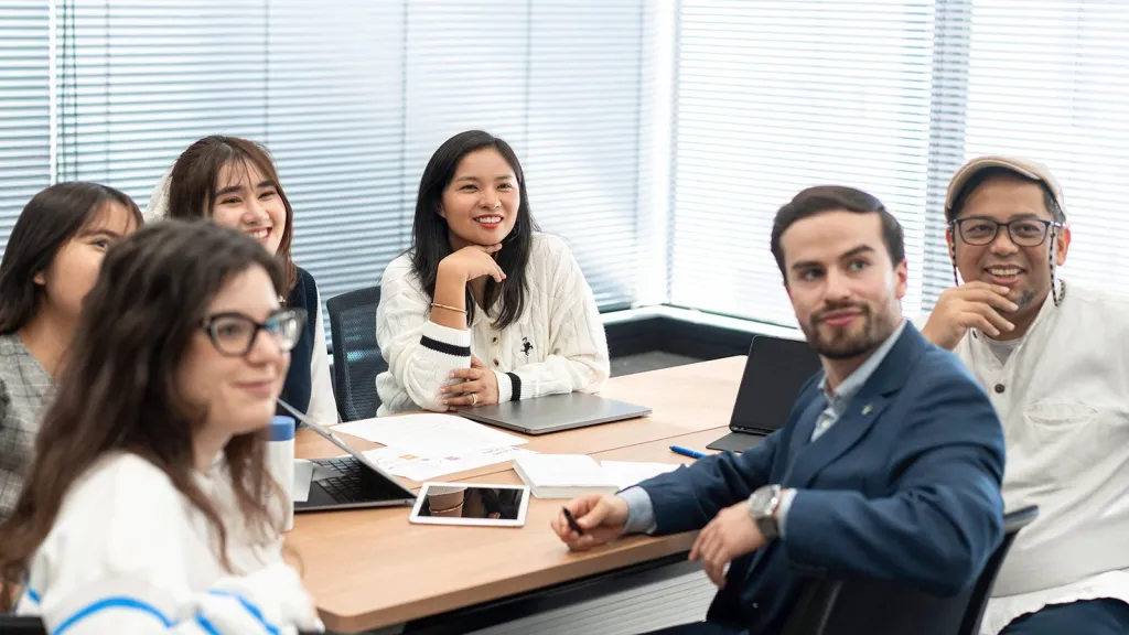 A diverse group of business students sitting around a conference table, smiling and participating in a group workshop.