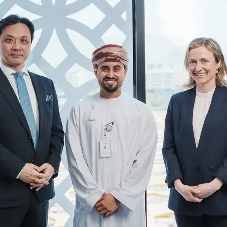 Three professionals in business and traditional Omani attire standing side-by-side in front of a large window.