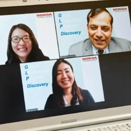 Laptop screen showing a three-person video call. Virtual backgrounds display Honda and GLP Discovery logos.   